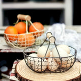 Outdoor table setting with a cream metal basket filled with bright, ripe oranges, and an unpainted metal basket filled with farm fresh eggs.