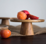 Wooden cake stand has apples and persimmons on it.
