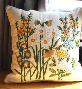 Cream pillow with embroidered daisies, blue flowers, yellow flowers, and green stems and leaves.