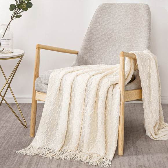 Cream blanket is draped over a beige and wood chair. Next to it is a table with a plant.