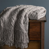 Light grey throw blanket is folded and placed on top of a dark wooden dresser.