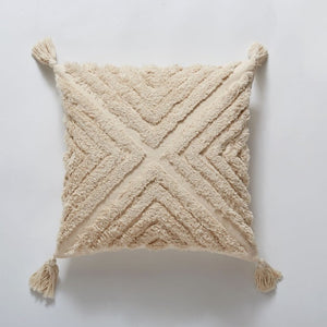 Boho cream pillow with a cream tassel in each corner. An X runs from corner to corner, dividing the pillow into four triangles that are each full of textured lines.