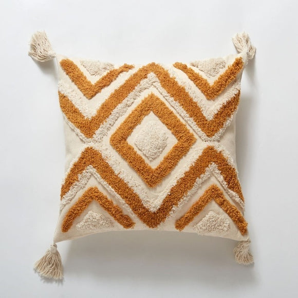 Boho cream pillow with a cream tassel on each corner. The pillow has a textured diamond and zig zag design in cream and a deep yellow/orange colour.